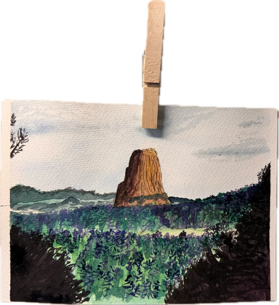 Watercolor painting of Devils Tower rising above dark pine forest and green hills, clipped to a string with a wooden clothespin.